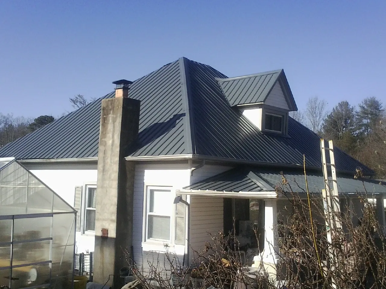 Dark blue standing seam metal roof on a white farmhouse with dormer — Slate & Tile Roof Repair by Roofing Brothers in Yankeetown