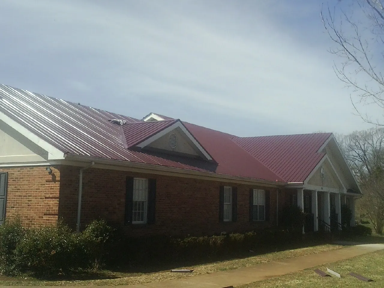 Red metal roof with gabled entries on a long brick building, from a Hail Damage Roof Repair job in Yankeetown