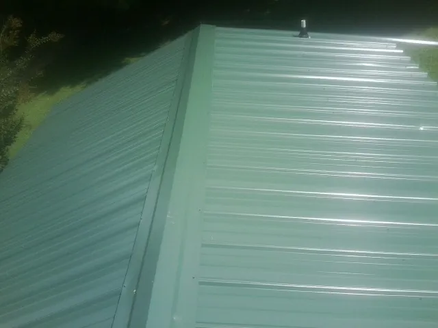 New green metal panels meeting at the ridge of a roof — Flat Roof Repair work by our crew in Yankeetown