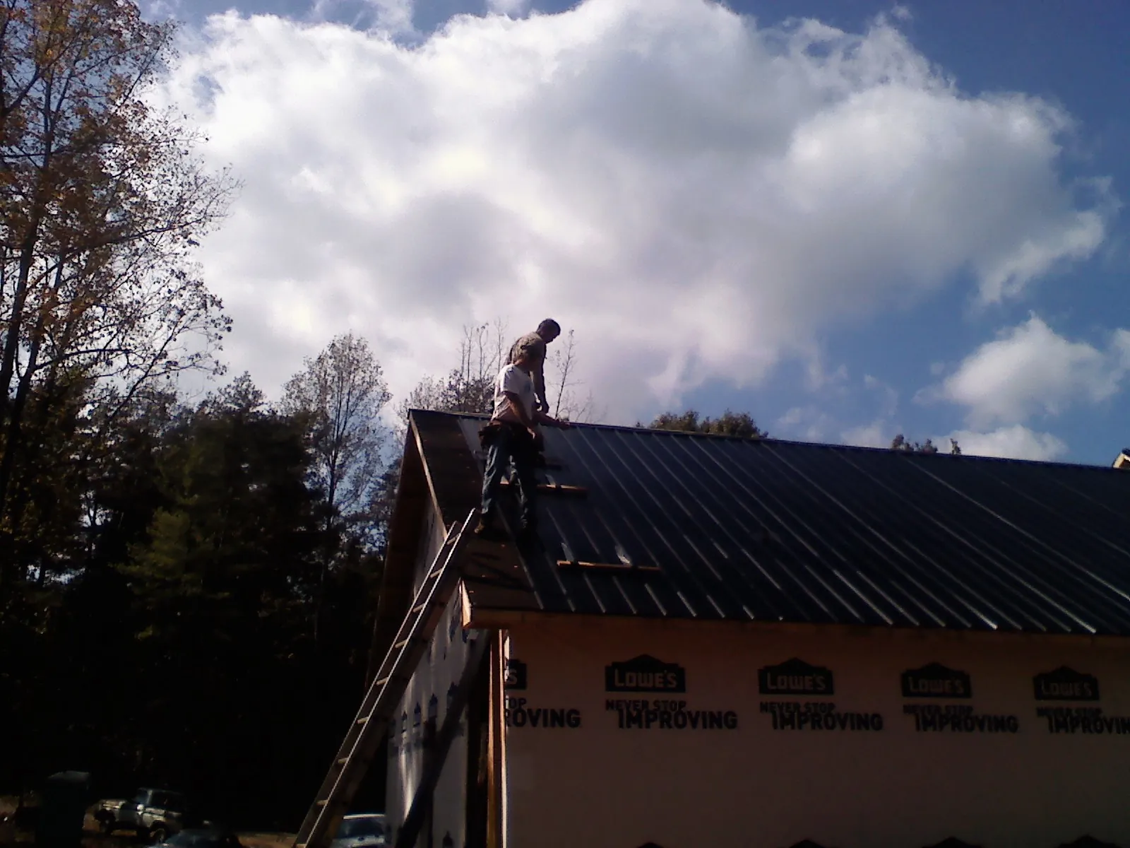 Roofer fastening dark metal panels high against a cloudy sky, from a Roof Inspection job in Yankeetown