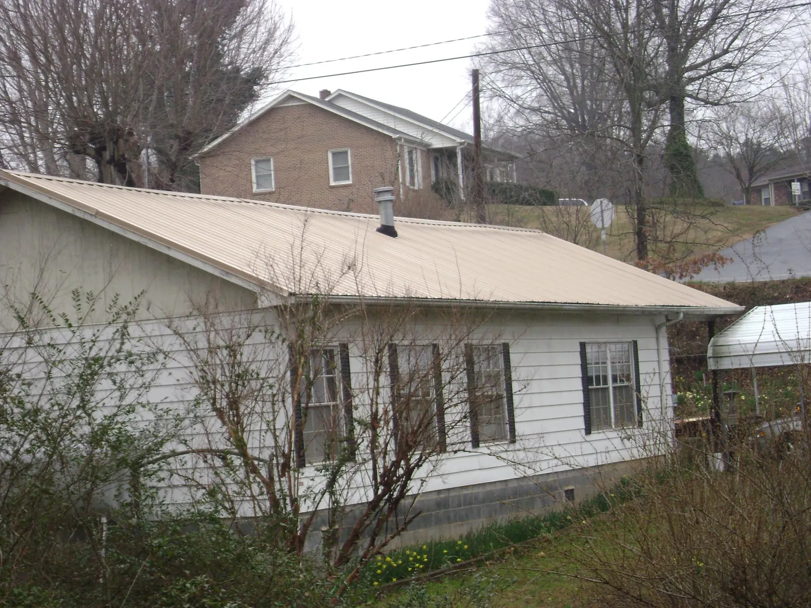 Tan metal roof on a white sided house set into a hillside — Commercial Roofing by Roofing Brothers in Yankeetown